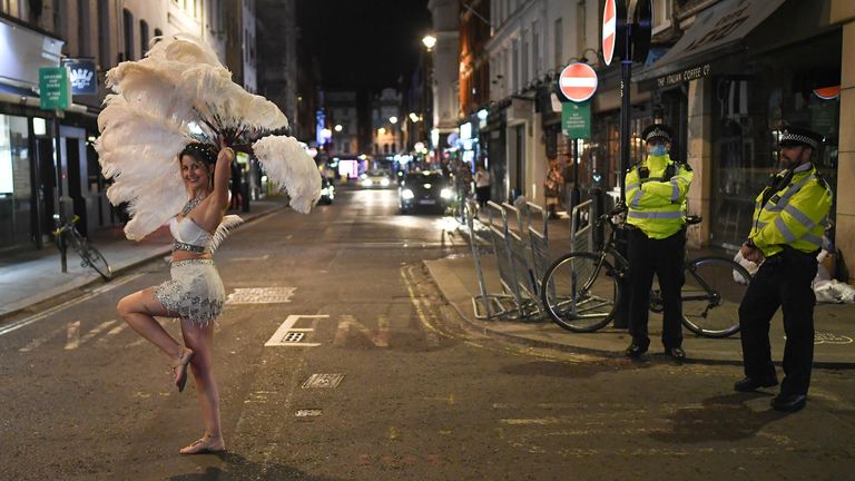 Police look on as an entertainer walks past in Soho