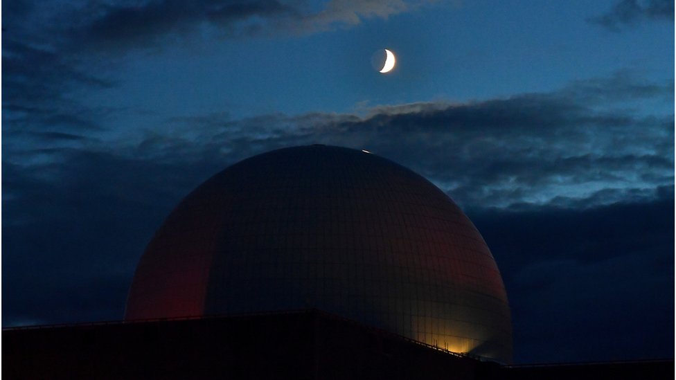 White domed nuclear power plant under a dark sky with crescent moon