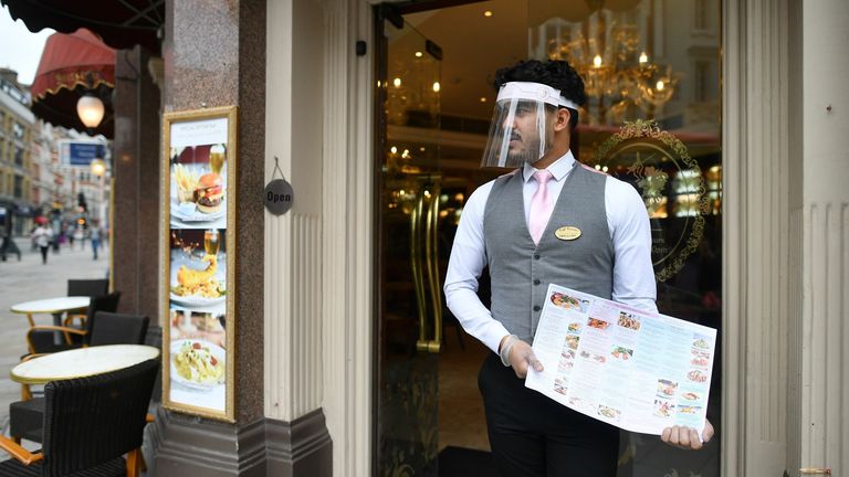 A restaurant employee stands on the step of a restaurant with a menu in the Soho area of London on July 4, 2020, as restrictions are further eased during the novel coronavirus COVID-19 pandemic. - Pubs and restaurants in England reopen on Saturday for the first time since late March, bringing cheer to drinkers and the industry but fears of public disorder and fresh coronavirus cases. (Photo by JUSTIN TALLIS / AFP) (Photo by JUSTIN TALLIS/AFP via Getty Images)